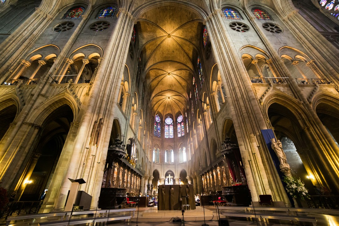 Vaulted stone ceilings, tall columns and stained-glass windows inside Notre Dame in Paris.