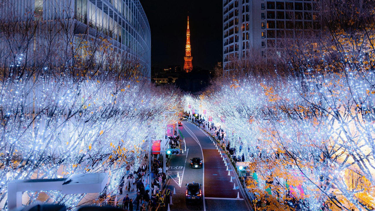 Tokyo Tower glowing orange beyond an avenue lined with blue and white winter lights.